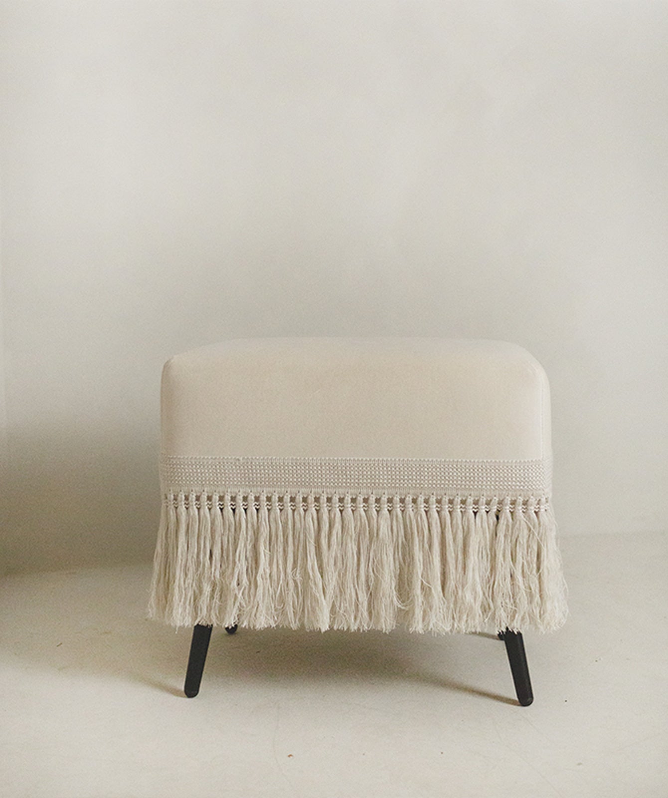 Upholstered cream velvet stool with soft rounded edges and trim detail