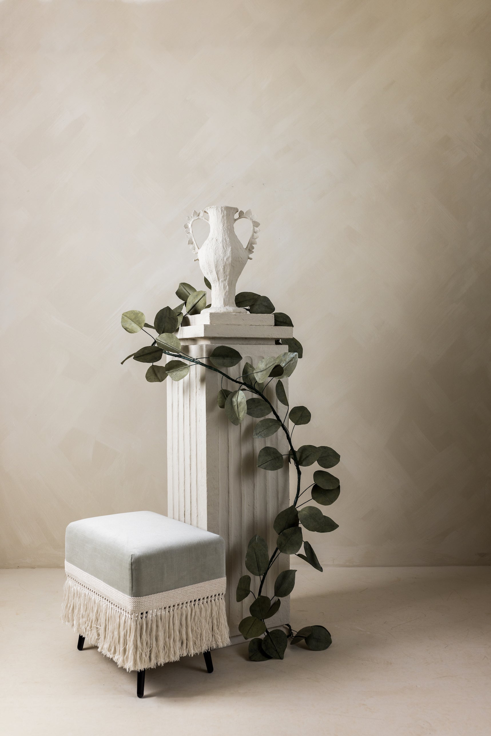 Verdigris velvet stool styled with fluted column and eucalyptus branches in neutral 
