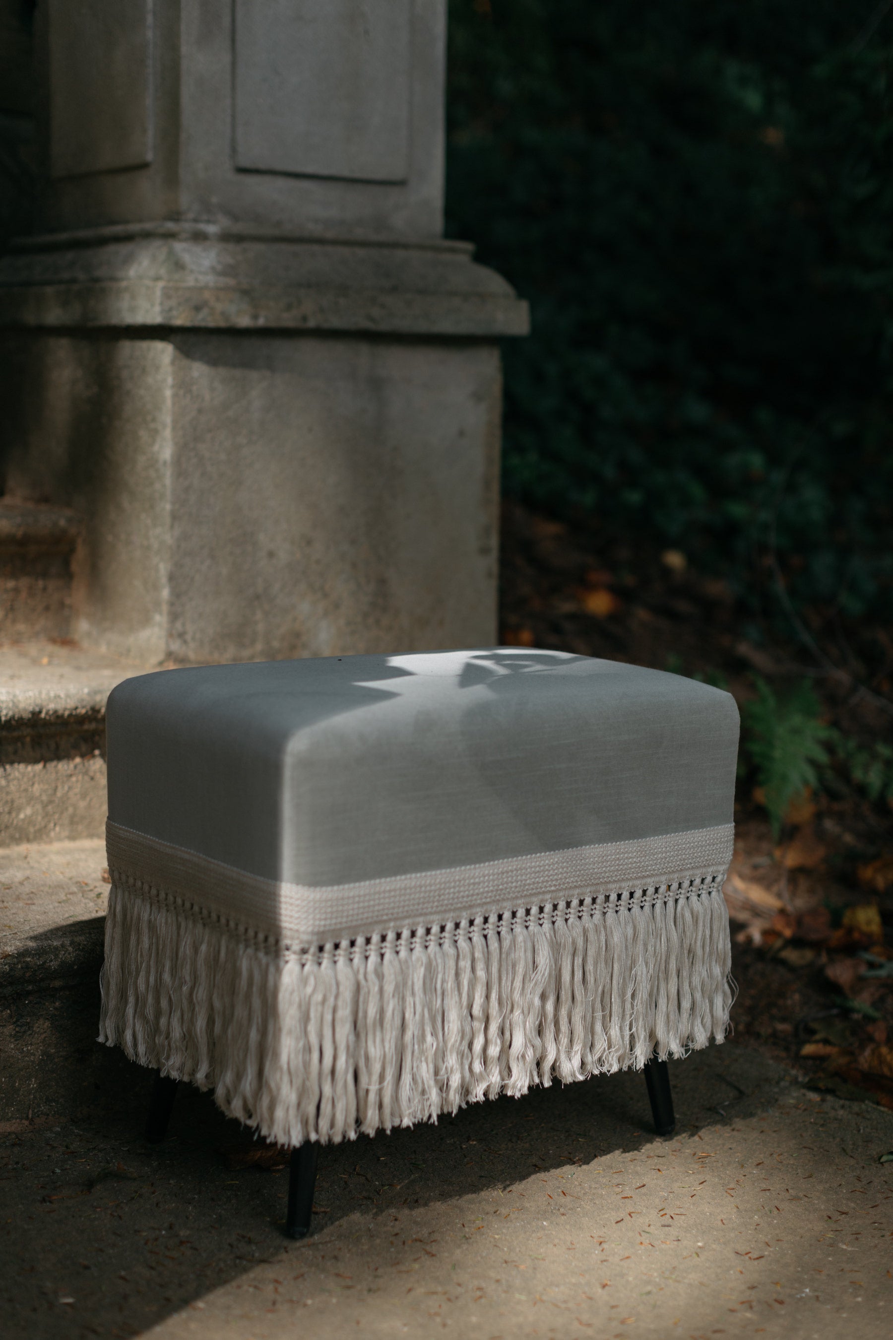 Verdigris stool with fringe trim photographed outdoors on stone steps with natural lighting
