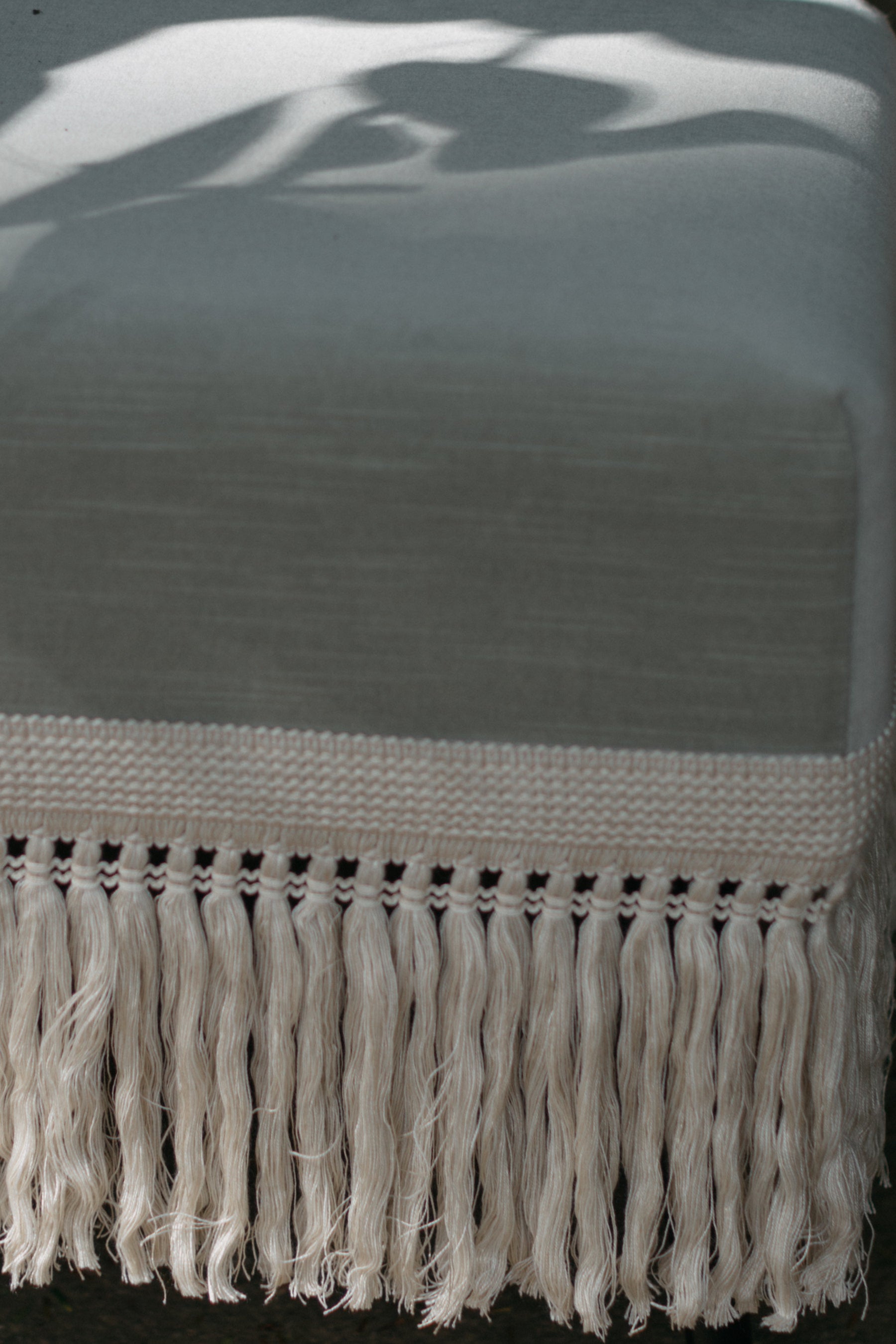 Detail shot of Verdigris stool handcrafted ecru fringe trim with dramatic shadow patterns