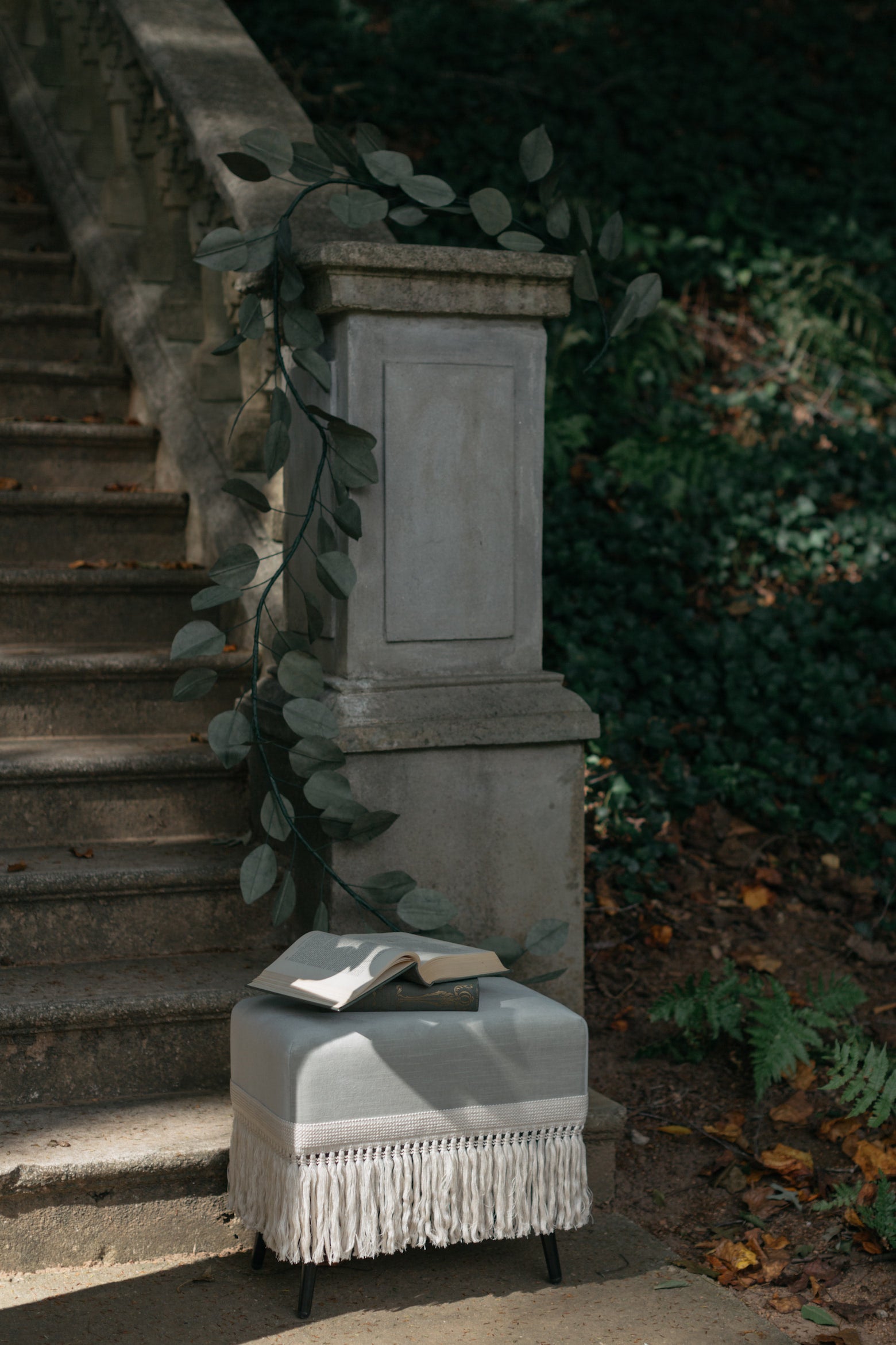 Verdigris velvet stool with fringe trim styled outdoors with open book and greenery